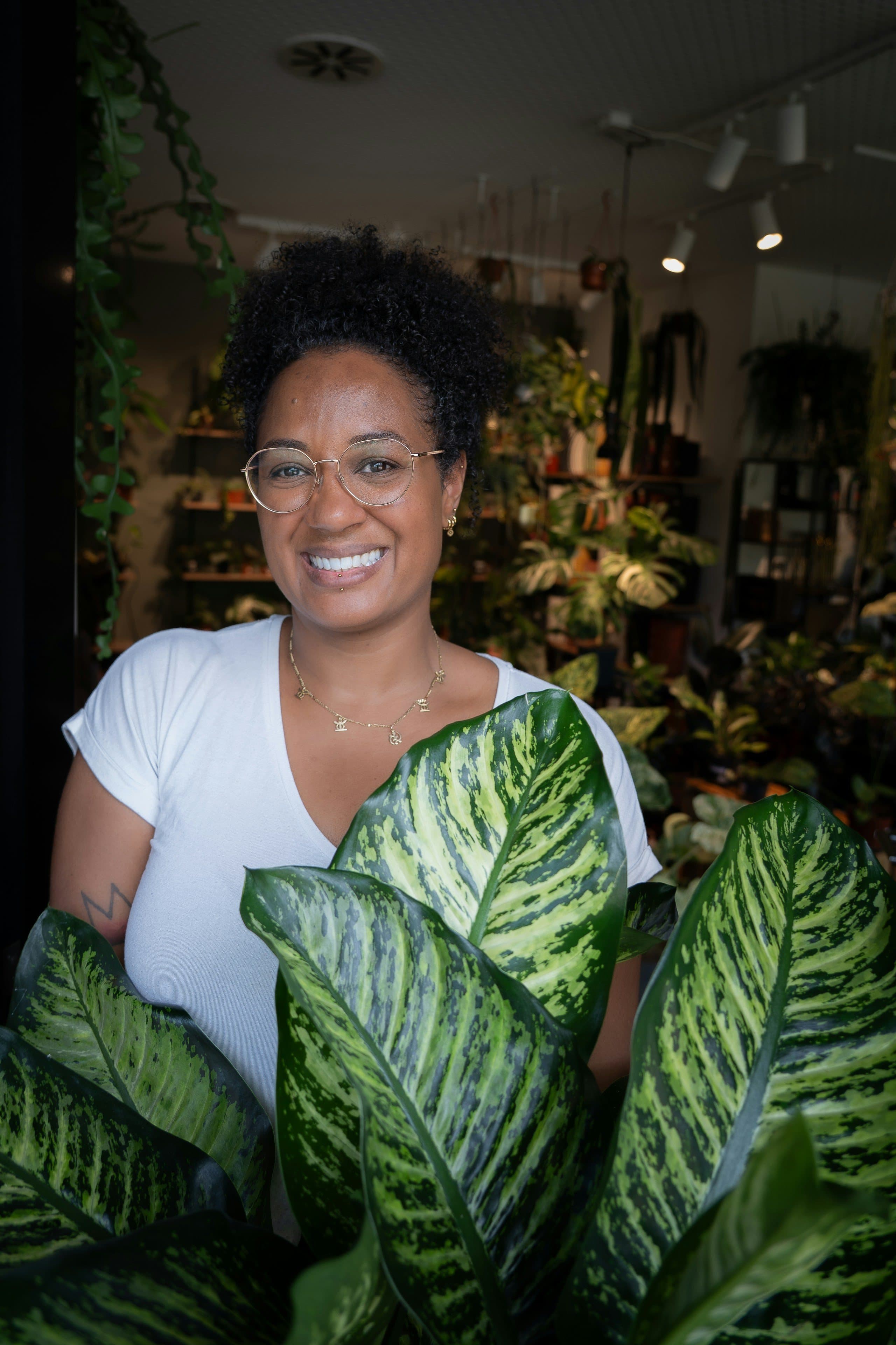 A smiling plant-shop owner holding a large leafy plant in her shop